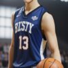 「BKSTY 13」と書かれたネイビーのユニフォームを着た若い男性が体育館でバスケットボールを持って立っている。 / A young man wearing a navy "BKSTY 13" basketball uniform is standing in a gym holding a basketball.