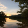 夕暮れの山奥に静かに広がる湖と、その水面に映る空と木々の風景。 / A tranquil lake deep in the mountains at sunset, reflecting the sky and trees on its surface.