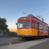 夕暮れの空の下、赤と黄色の路面電車が道路脇に停車している風景。 / A red and yellow streetcar stopped beside the road under the evening sky.