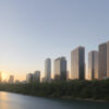川の向こうに高層ビルが並び、手前には緑豊かな木々が広がる都市の風景。 / A cityscape with tall buildings across the river and lush trees in the foreground.