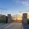 夕陽に照らされる洋風デザインの校門が堂々と建つ風景。 / A grand Western-style school gate illuminated by the setting sun.