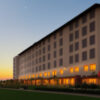 夕暮れの空の下、明かりの灯った中層ホテルが静かに佇む風景。 / A mid-rise hotel with glowing windows standing quietly under the twilight sky.
