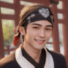 バンダナを頭に巻いた若い男性が、和風の建物の前で笑顔を見せている。/ A young man wearing a bandana around his head is smiling in front of a traditional Japanese building.