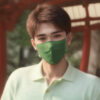 緑色のマスクを着けた若い男性が緑のポロシャツを着て屋外で微笑んでいる。 / A young man wearing a green mask and a green polo shirt is smiling outdoors.