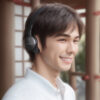 黒いワイヤレスヘッドホンを着けて笑顔を見せる若い男性。 / A young man smiling while wearing black wireless headphones.