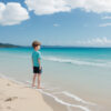 穏やかな砂浜を眺める青いシャツの少年 / A boy in a blue shirt gazing at the calm sandy beach