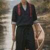 木製カヌーに立つ青年が赤いパドルを手に微笑む、夕暮れの湖畔での一コマ A young man standing in a wooden canoe with a red paddle, smiling by a lakeside at dusk