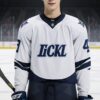 白と紺のアイスホッケーユニフォームを着た青年が正面を見つめて立つ A young man in a white and navy ice hockey uniform standing and looking straight ahead