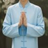 桜の木の下で合掌のポーズをとる青年、淡い水色の気功服を着用 A young man in pale blue qigong wear performing a prayer pose beneath a cherry blossom tree