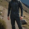 黒とグレーのトレッキングウェアを着た青年が山道を歩きながら微笑む A young man in black and gray trekking wear smiling while walking along a mountain trail