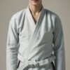 白帯の柔道着を着て正面を見つめる若い男性。落ち着いた背景の中で微笑んでいる。/A young man wearing a judo uniform with a white belt, smiling and facing forward against a calm background.