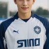 白と青の「SINO」ユニフォームを着た若い男性がサッカー場でカメラを見つめている。 / A young man in a white and blue "SINO" soccer uniform is looking at the camera on the soccer field.