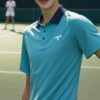 ブルーのテニスウェアを着た若い男性がテニスコートでラケットを持ち、微笑んでいる。 / A young man in blue tennis wear is smiling while holding a racket on the tennis court.