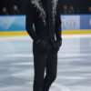 黒にシルバーの装飾が施されたスケートウェアを着た若い男性が氷上で微笑んで立っている。 / A young man in black ice skating wear with silver decorations is smiling while standing on the ice.