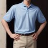 Young man wearing a light blue polo shirt and beige shorts, standing with both hands on his hips against a plain background （薄青のポロシャツとベージュのショートパンツを着た若い男性が、無地の背景の前で両手を腰に当てて立っている）