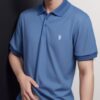 Young man in a blue polo shirt casually placing one hand on his stomach, looking slightly to the side （青いポロシャツを着た若い男性が片手をお腹に当て、少し横を見つめている）