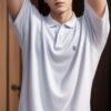 Young man in a white polo shirt with both arms raised behind his head, standing indoors （白いポロシャツを着た若い男性が、両腕を頭の後ろに上げて室内で立っている）