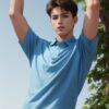Young man in a light blue polo shirt stretching both arms upward under a tree （ライトブルーのポロシャツを着た若い男性が木の下で両腕を上に伸ばしている）