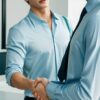 Two young businessmen in shirts shaking hands in a modern office （シャツ姿の若いビジネスマン2人が、モダンなオフィスで握手している）