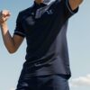 Young man in a navy polo shirt striking a victory pose with fist raised against a blue sky （紺色のポロシャツを着た若い男性が、青空に向かって拳を突き上げる勝利のポーズを取っている）