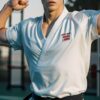Young man in a white karate gi striking a strong double-arm pose outdoors （白い空手着を着た若い男性が、屋外で両腕を力強く構えるポーズ）