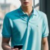 Young man in a light blue polo shirt casually operating a smartphone with one hand on a balcony （薄い水色のポロシャツを着た若い男性がバルコニーで片手にスマートフォンを持ち操作している）