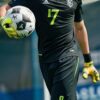 Young male goalkeeper in black uniform preparing to throw a soccer ball with one hand （黒いユニフォームを着た若いゴールキーパーが片手でサッカーボールを投げようとしている）