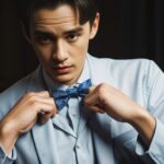 淡いブルーのシャツを着た男性が蝶ネクタイを結んでいるクローズアップ写真。 / A close-up photo of a man in a light blue shirt tying a bow tie.