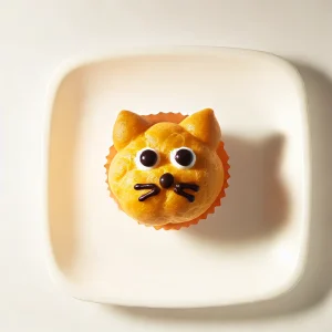 お皿にのせられた猫型シュークリーム、手のひらサイズの可愛らしいスイーツ Cat-shaped cream puff served on a plate, a palm-sized and adorable dessert
